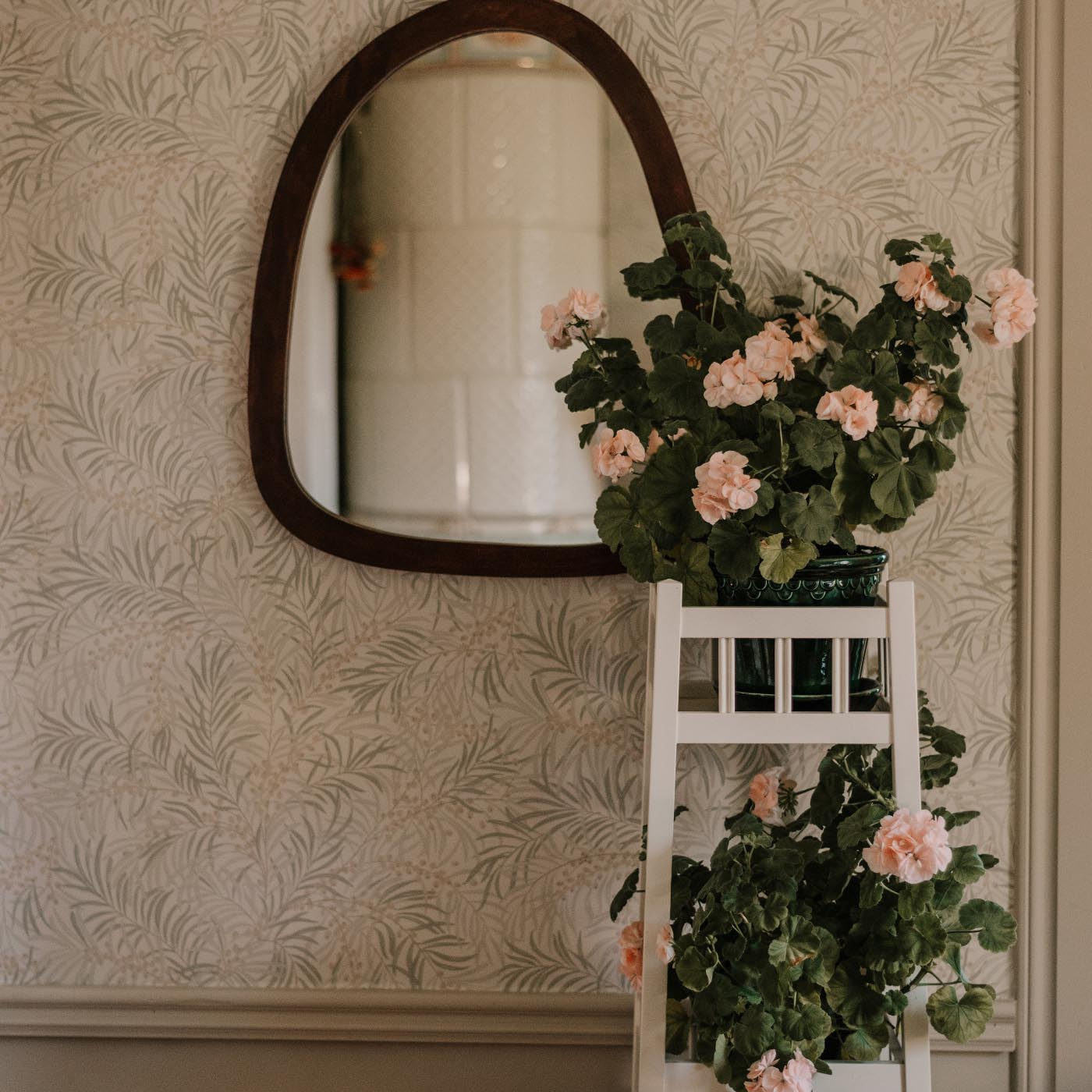 Vit piedestal i trä framför spegel med grön växt 