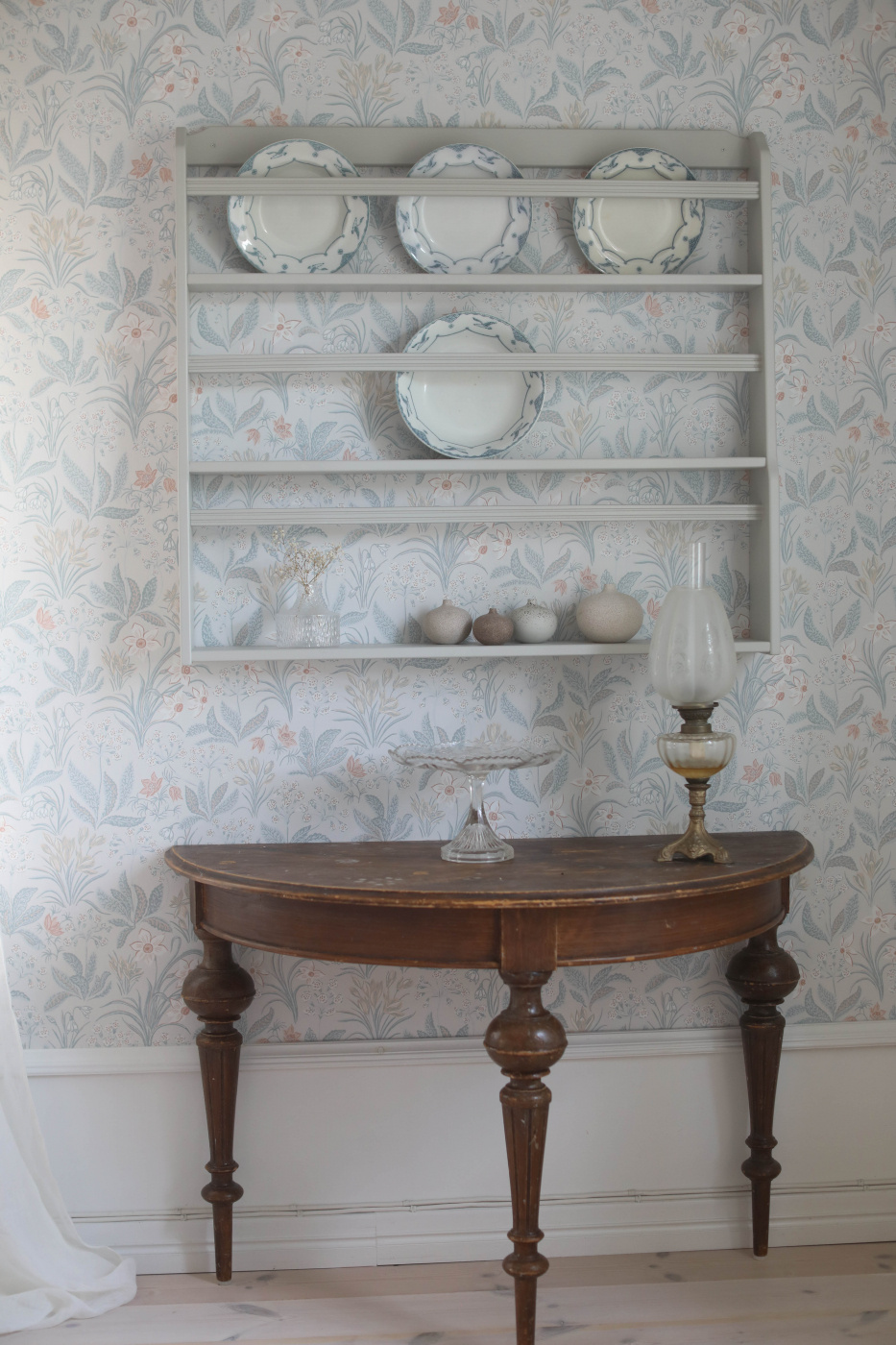 Tallrikshylla på väggen i ett ljus hem med porslin och dekorationer 