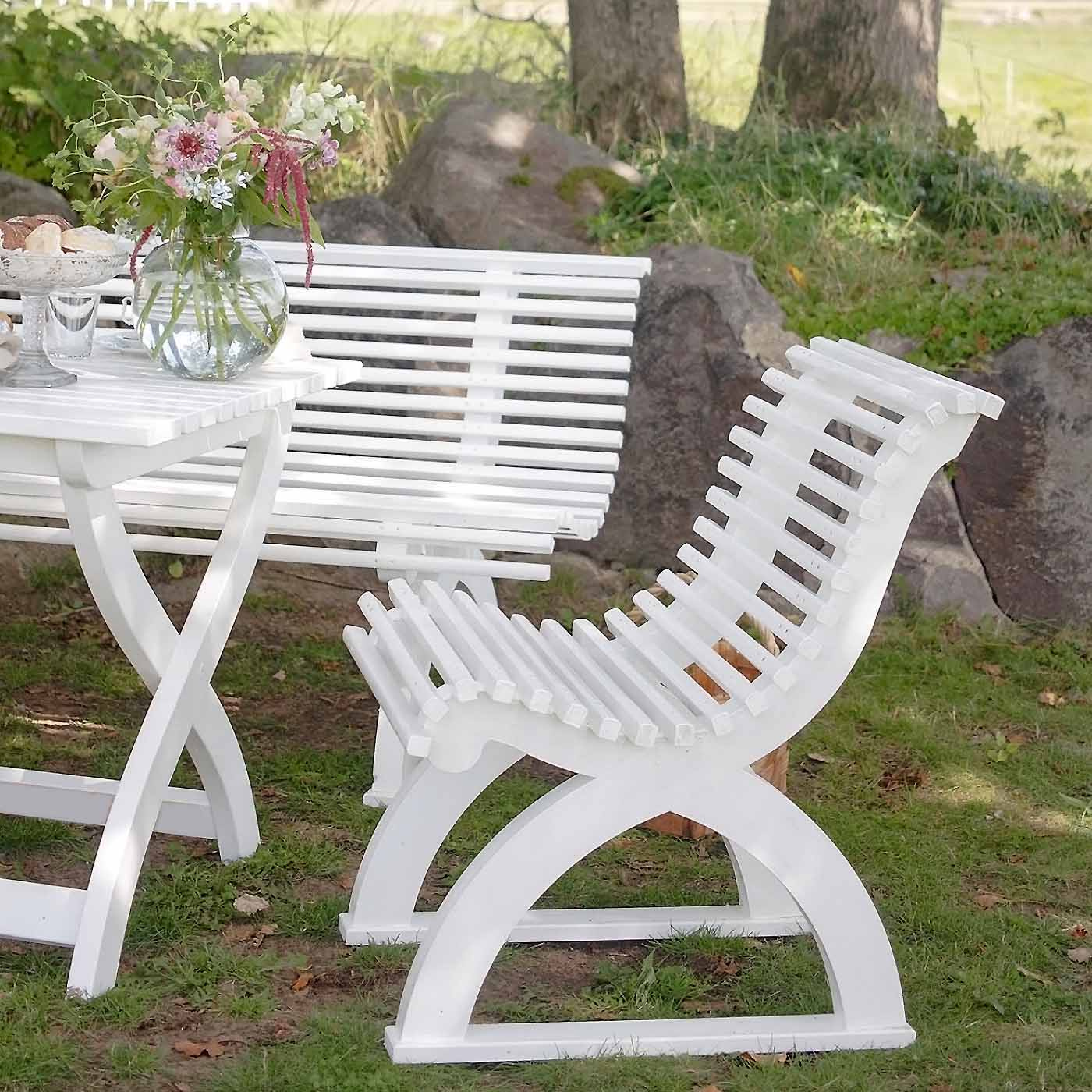 Vit trädgårdsstol vid utemöbel med vas och blommor på bordet 