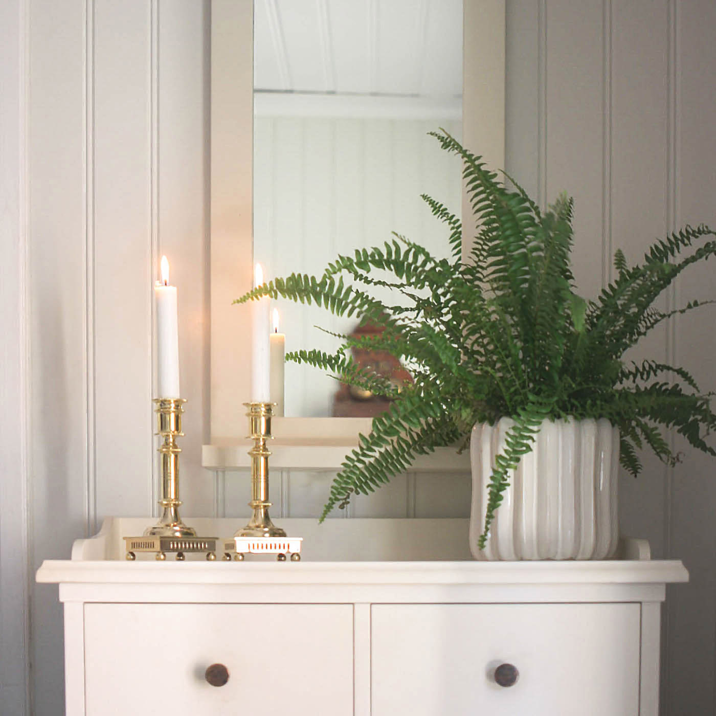 Två mässingsljusstakar med kulfötter framför grön krukväxt 