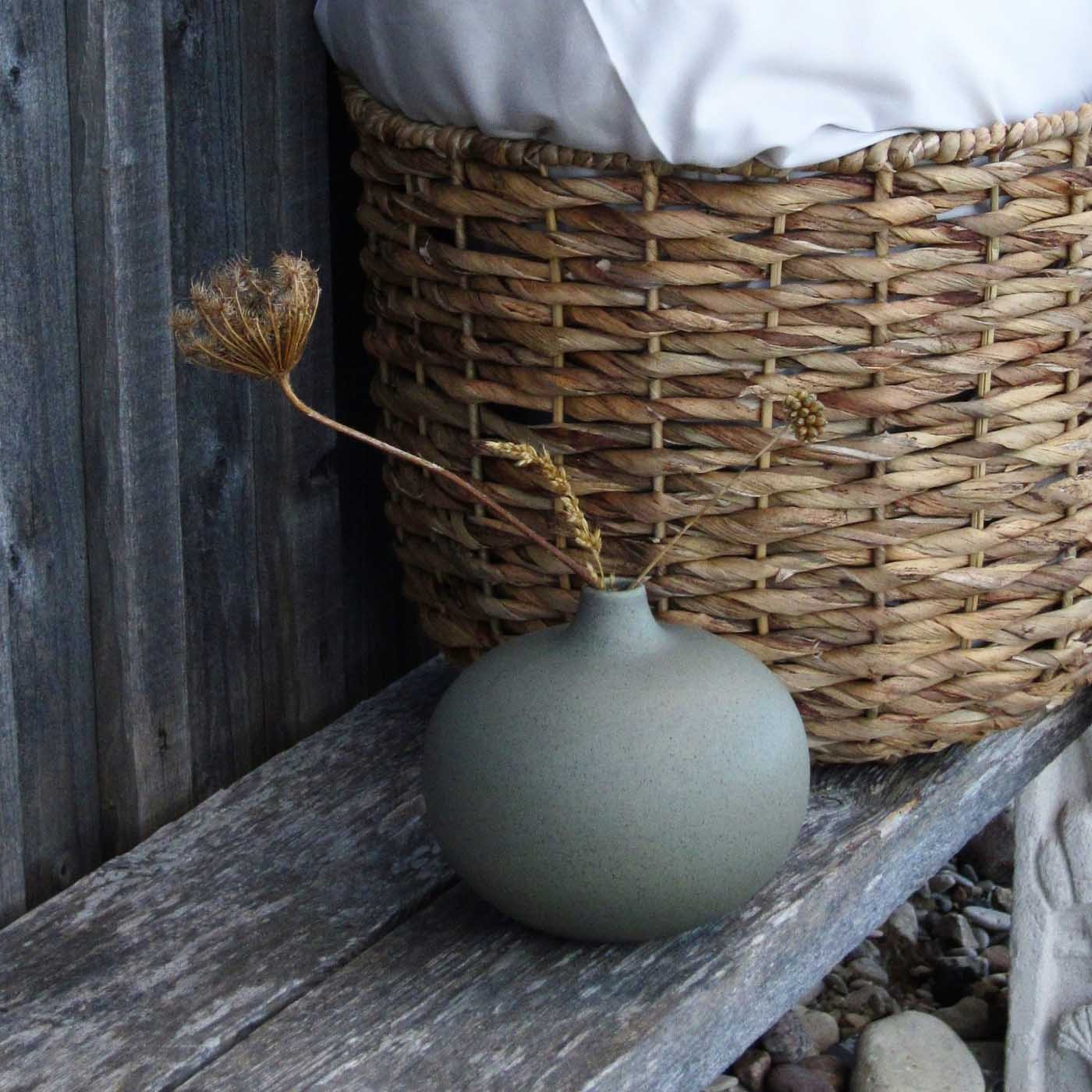 ChatGPT sade:  Grön vas på rustik bänk intill en flätad korg